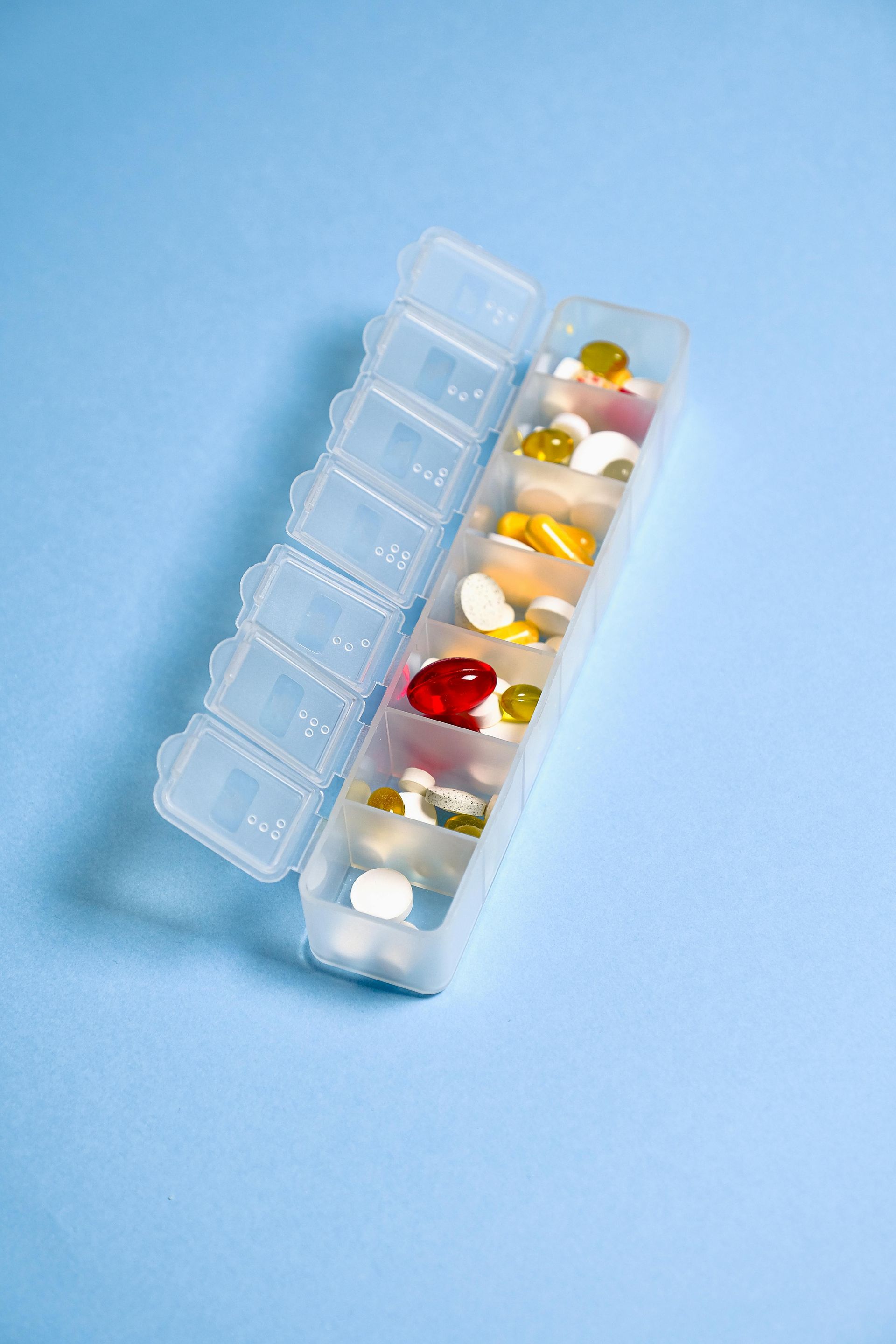A plastic, seven-day pill organizer with various colorful medications, angled on a plain blue background.