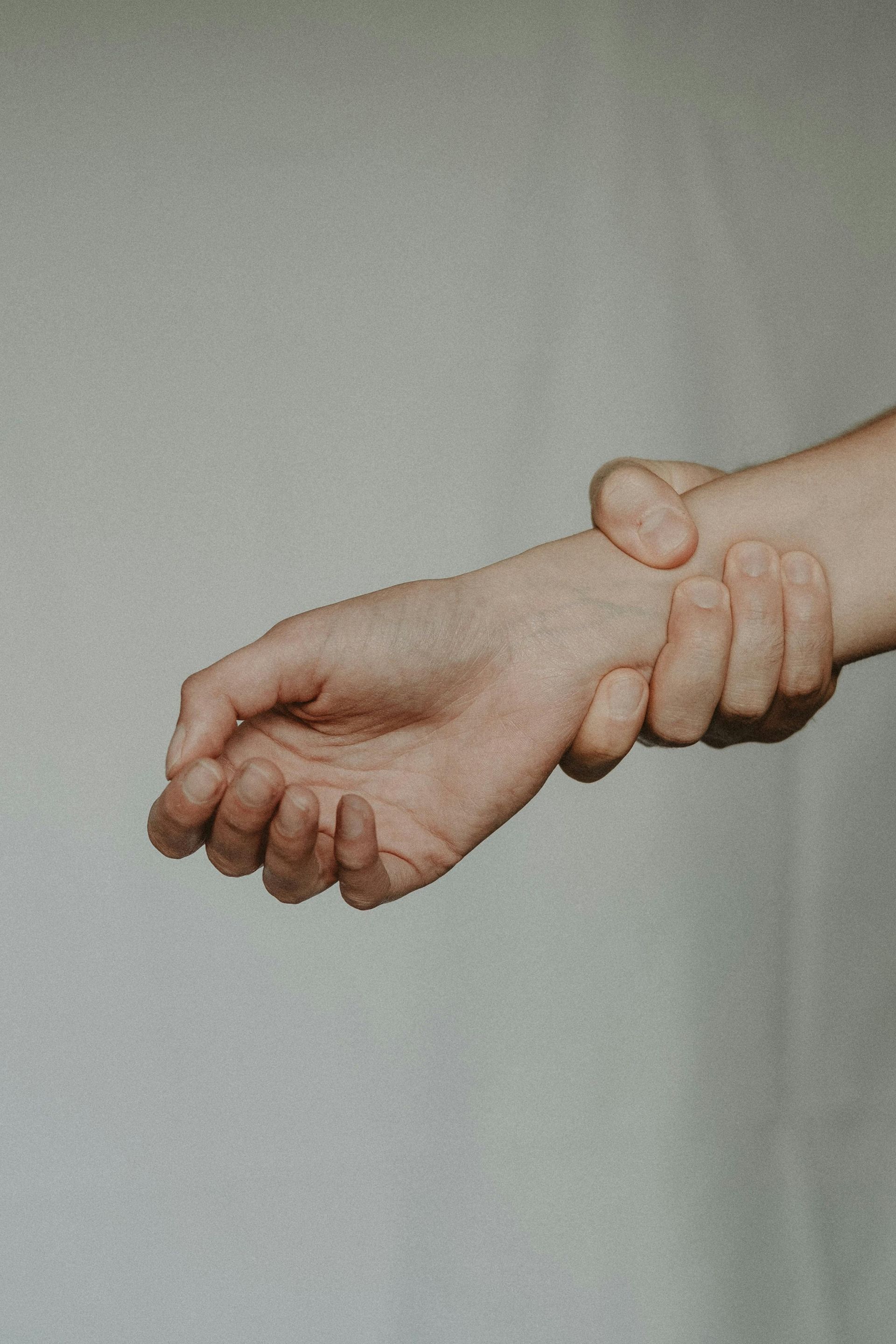 A hand firmly gripping another person's wrist against a plain, light-colored background.