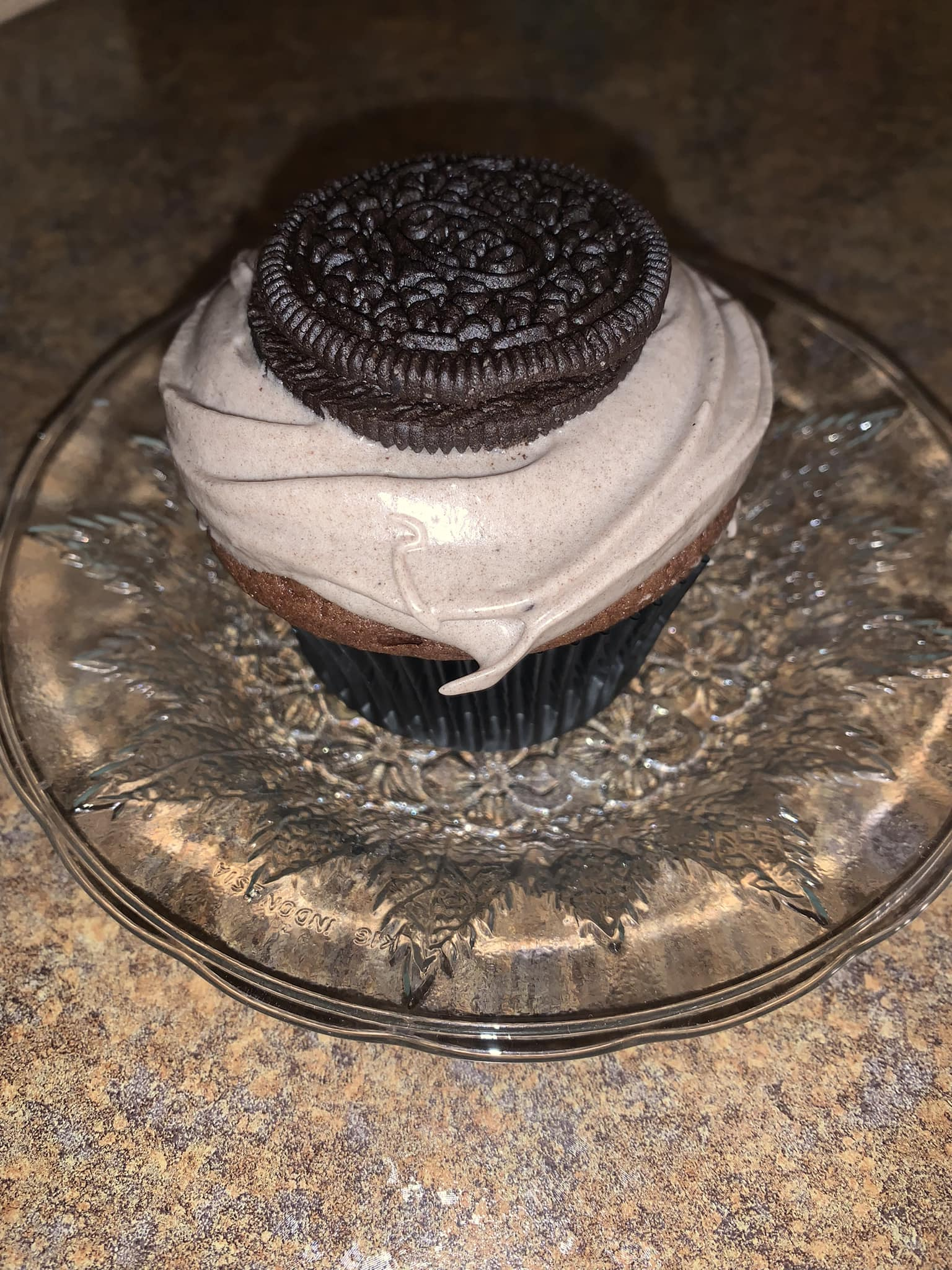 Cupcake with chocolate frosting and Oreo cookie on a glass plate.