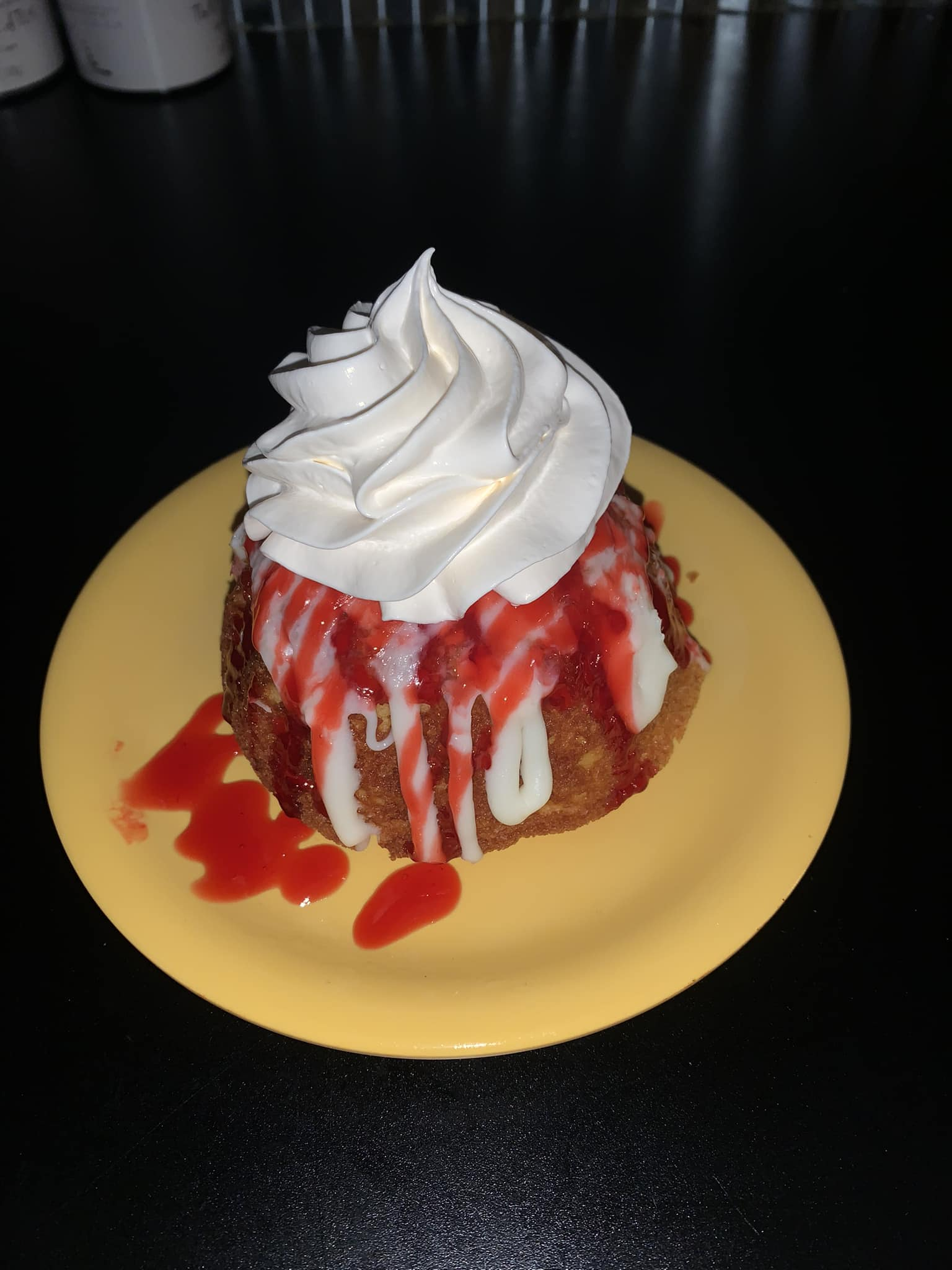 Dessert: fried pastry with strawberry sauce and whipped cream on a yellow plate.