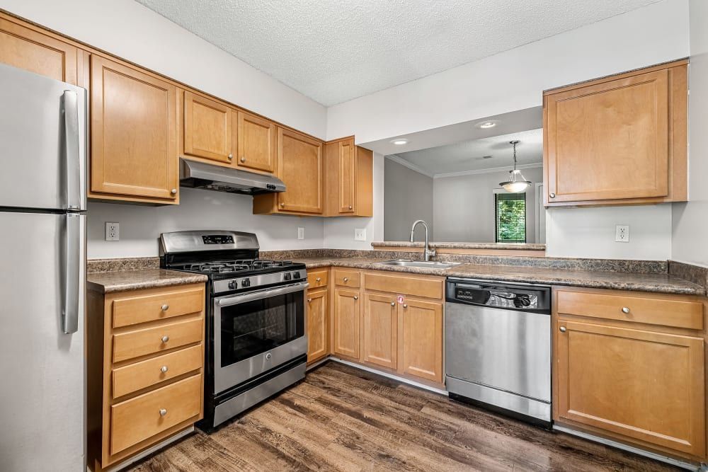 A side view of the apartment kitchen with stainless steel appliances, wooden cabinets, and a window at Marquis at Perimeter Center in Atlanta, GA.