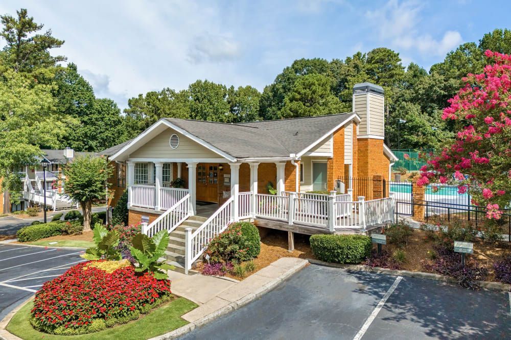 Trees and flowers surround the clubhouse with a porch and stairs at Marquis at Perimeter Center in Atlanta, GA.