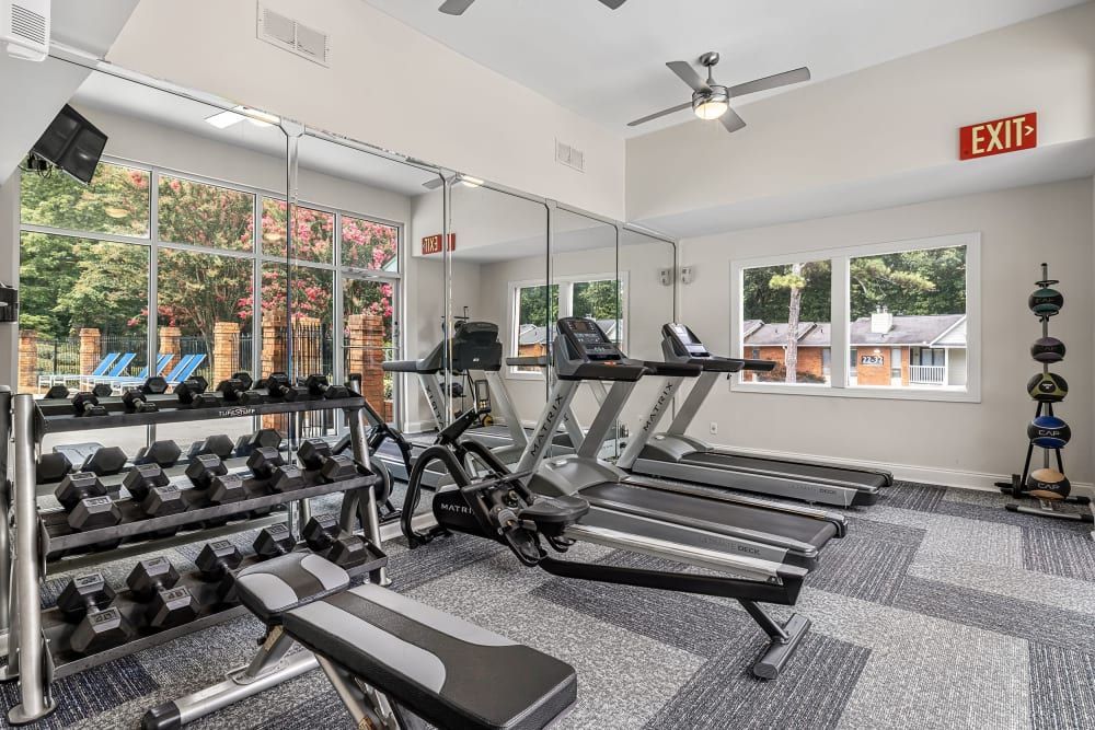 A gym with treadmills, dumbbells, a bench, and ceiling fans at Marquis at Perimeter Center in Atlanta, GA.