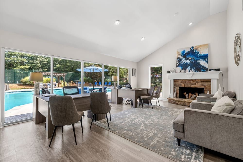 Spacious clubhouse with a desk, chairs, a couch, a fireplace, floor-to-ceiling windows, and beautiful pool views at Marquis at Perimeter Center in Atlanta, GA.