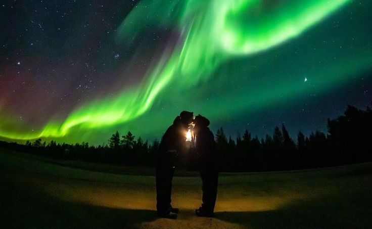 couples dressed in winter clothes standing under aurora sky in tromso