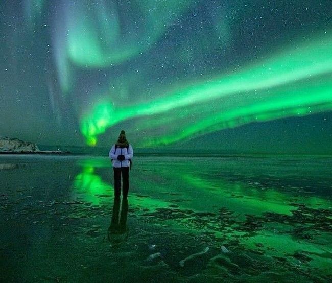 couples dressed in winter clothes standing under aurora sky in tromso