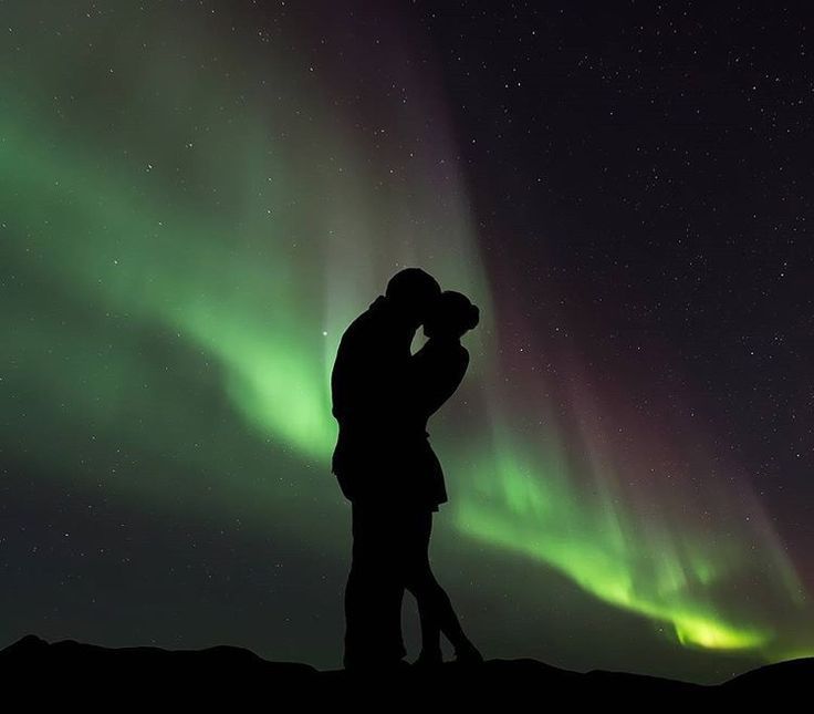 couples dressed in winter clothes standing under aurora sky in tromso and kissing each other