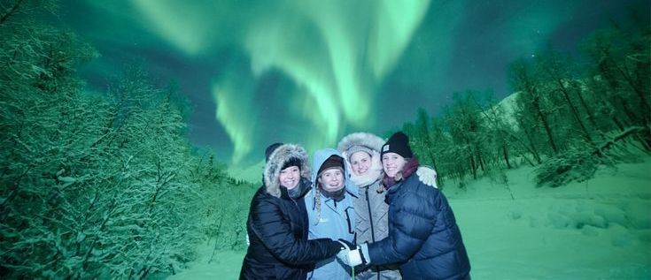 couples dressed in winter clothes standing under aurora sky in tromso