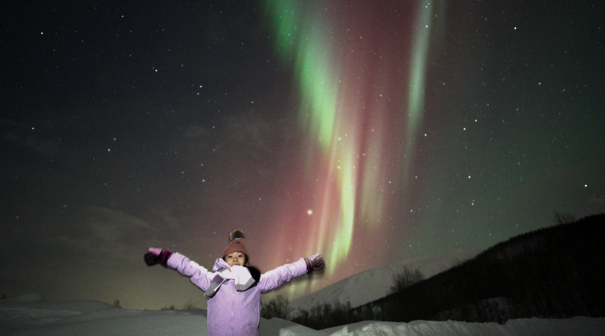 girl standing under aurora sky and northern lights colored in red and green