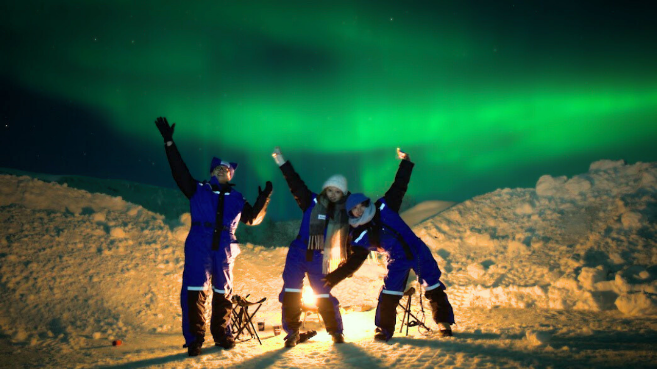 Group Tromso alshemal norway northern lights tour small group camp fire people waving under aurora sky