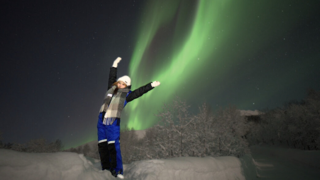 girl standing under aurora sky and northern lights colored in red and green dressed in winter clothes