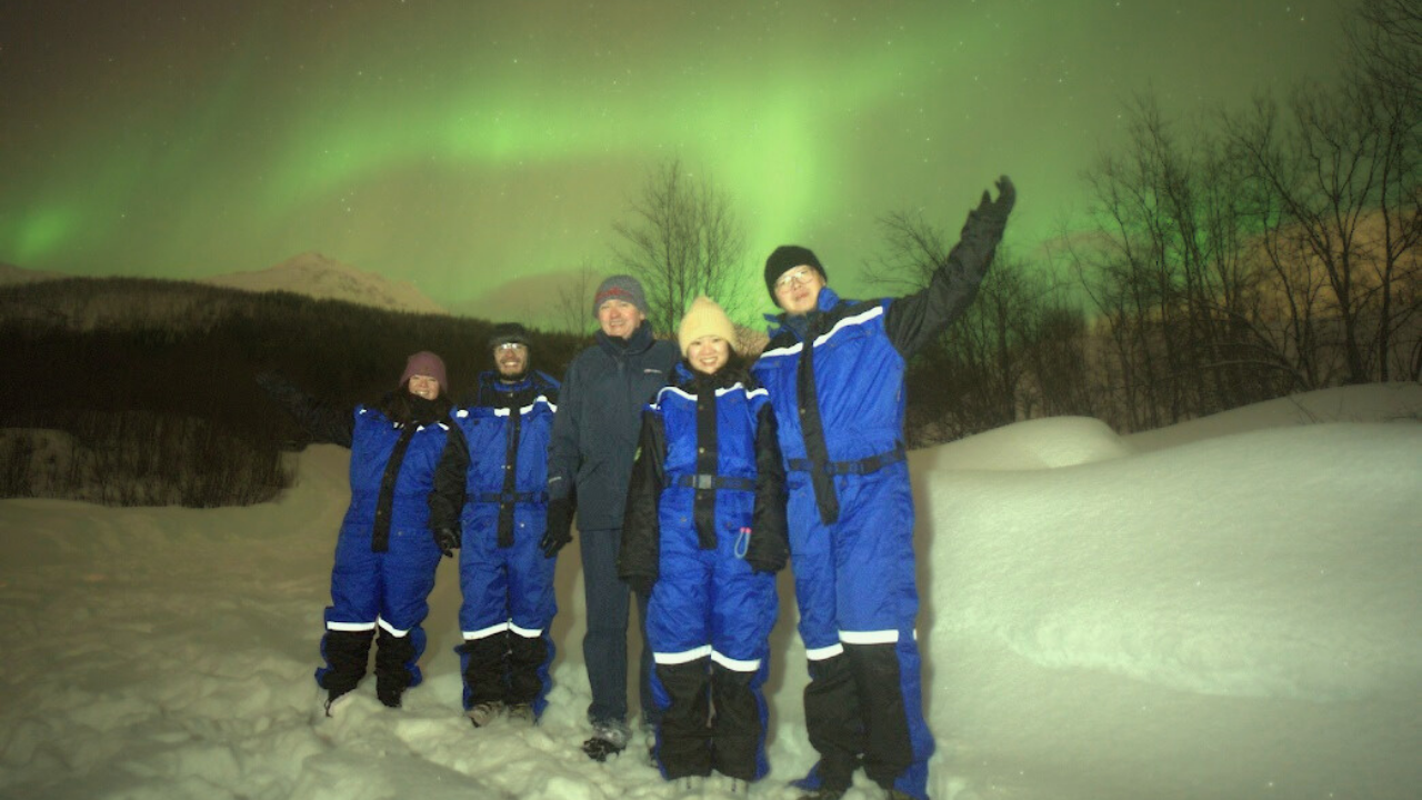 Group Tromso alshemal norway northern lights tour small group people waving under aurora northern lights sky