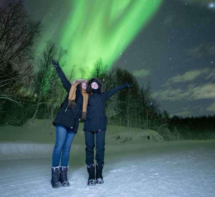 couples dressed in winter clothes standing under aurora sky in tromso