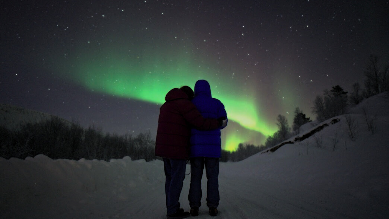 two couples satnding infront of northern lights in tromso dressed in winter clothing