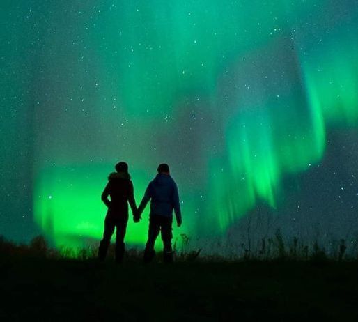 couples dressed in winter clothes standing under aurora sky in tromso