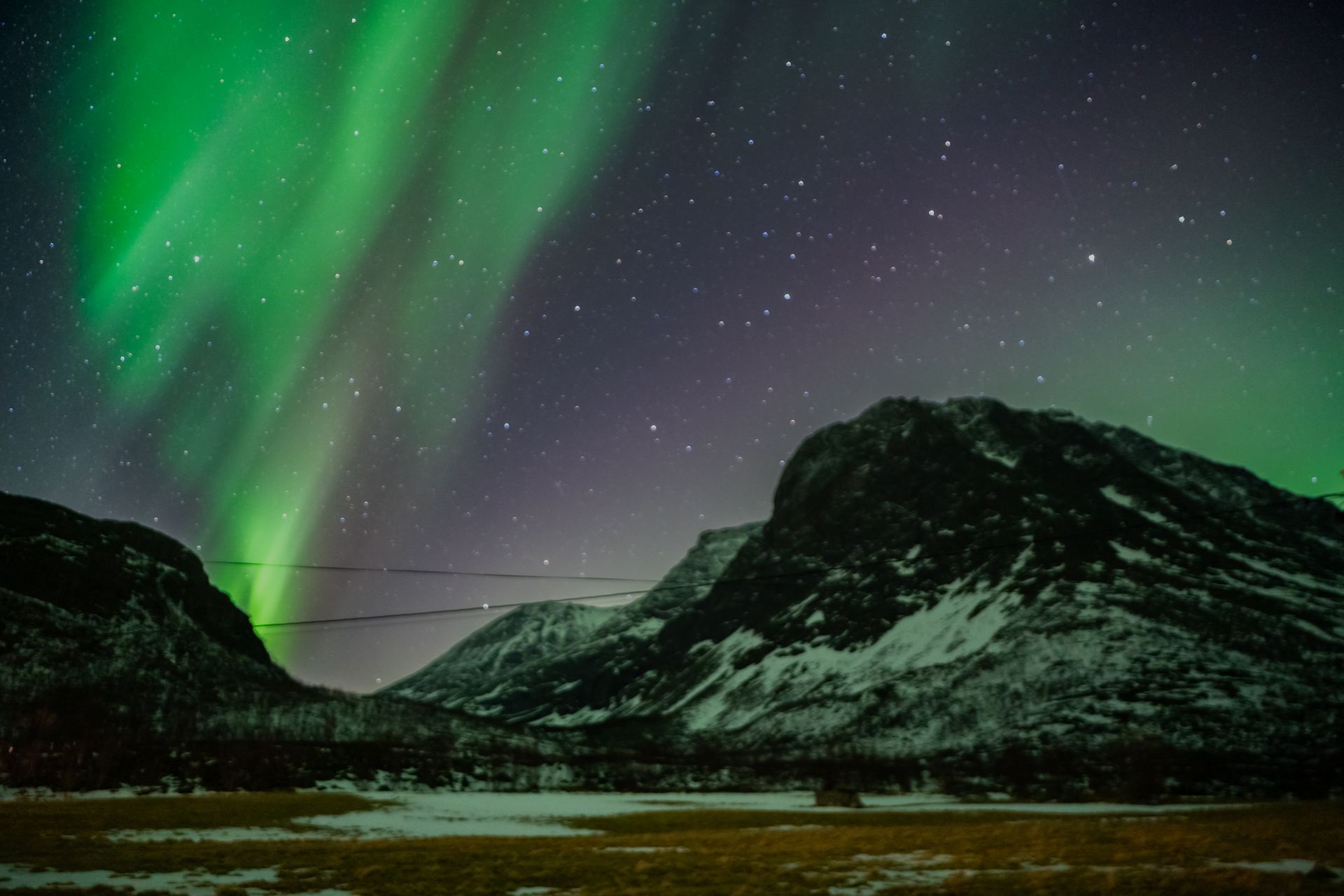 Green Northern Lights stretching across the Arctic sky above snow-covered mountains in Tromsø, photographed under real conditions without edits