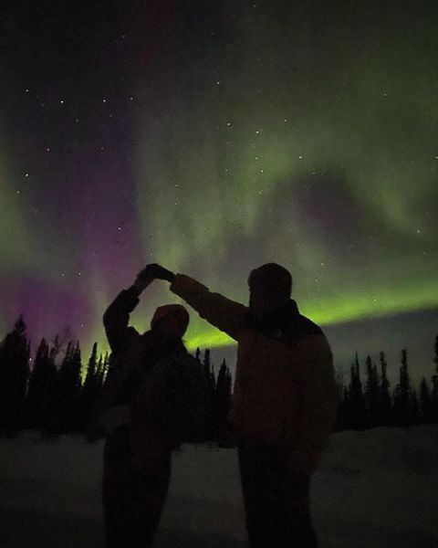 couples dressed in winter clothes standing under aurora sky in tromso