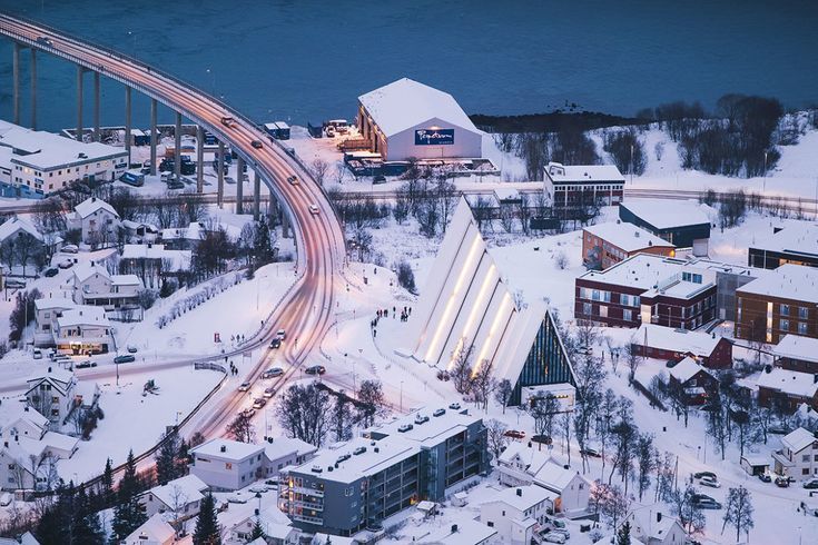 tromso cathedral and the road next to it covered in snow and the cars are showing verry small the photo is captured from the top of the mountain the bridge of tromso also showing and the sea as well
