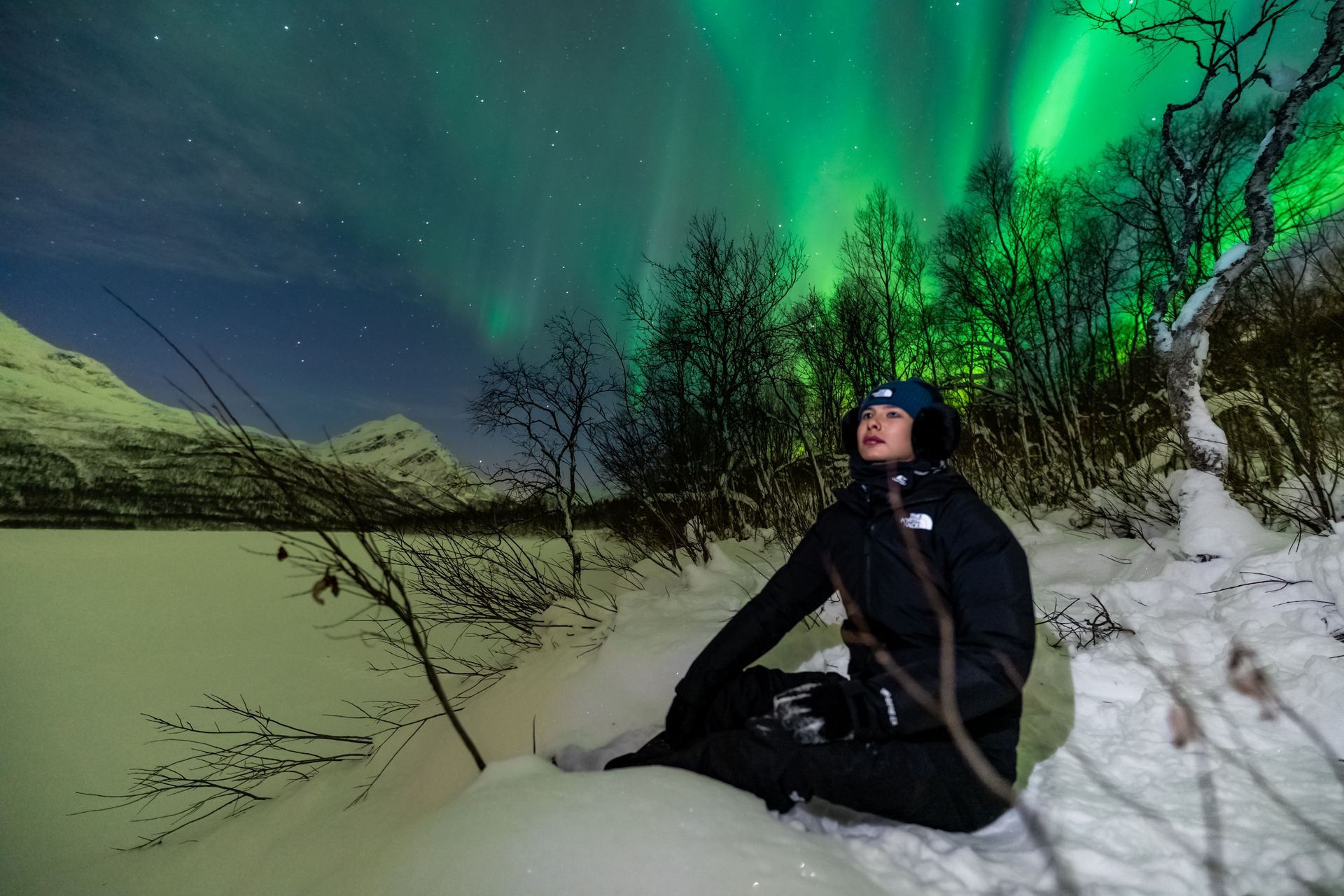 Guest sitting in snow watching Northern Lights Tromsø small group aurora tour winter Norway