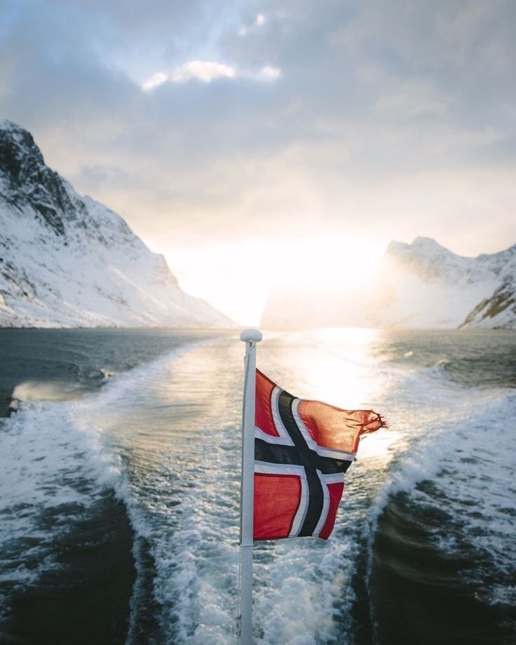 Norwegian flag over a ship and mountain and fjord covered in snow