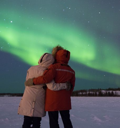 couples dressed in winter clothes standing under aurora sky in tromso