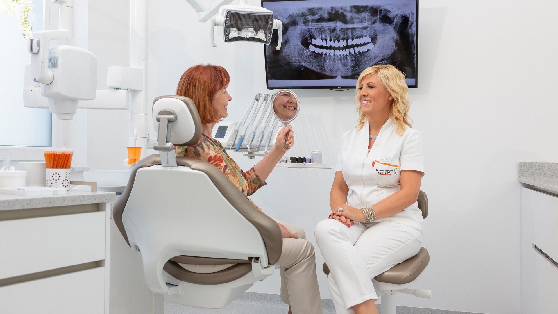 Una donna è seduta sulla poltrona del dentista e parla con un dentista.