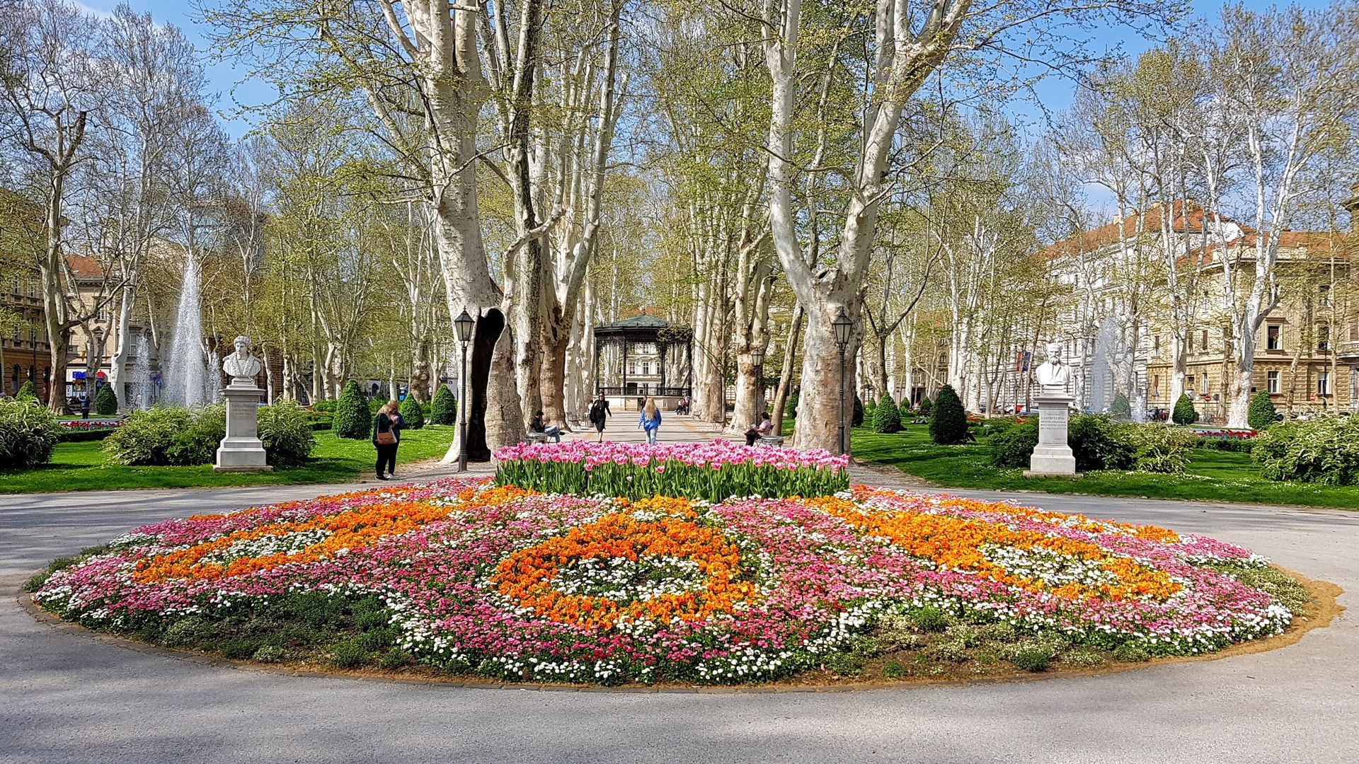 Un cerchio di fiori in un parco con una fontana sullo sfondo.