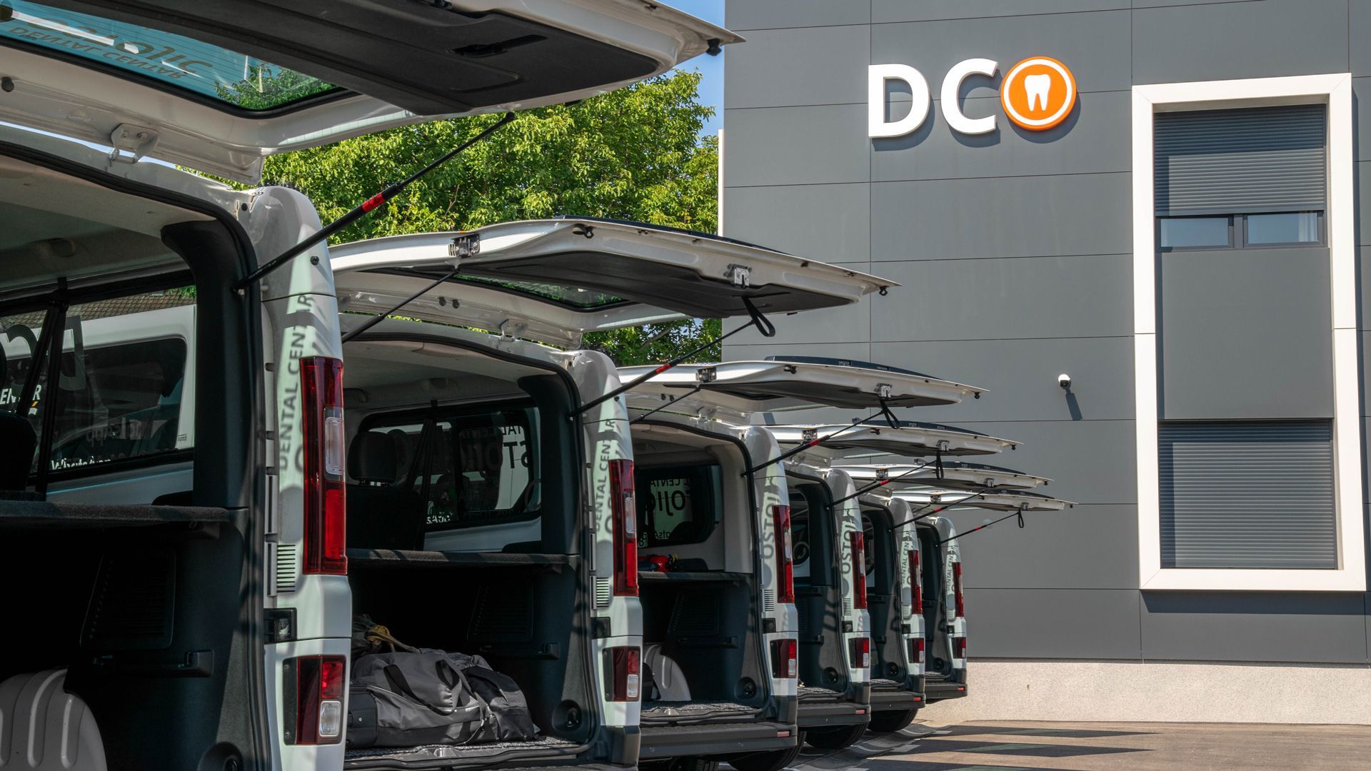 Una fila di furgoni parcheggiati davanti a un edificio con il bagagliaio aperto.