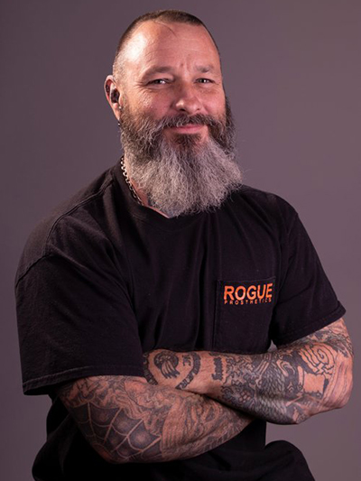 A man with a beard and tattoos is wearing a rogue t-shirt.