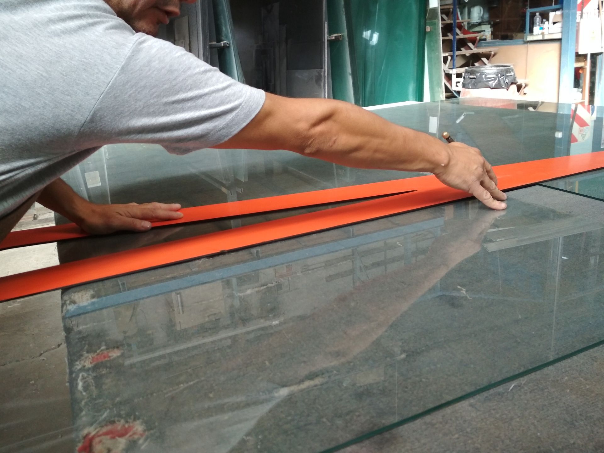 Un hombre corta un trozo de vidrio con una cinta naranja.