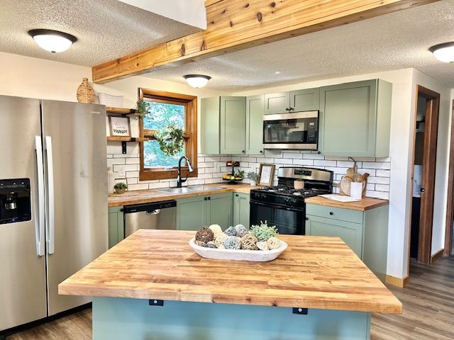 Kitchen with sage green cabinets, wood countertops, stainless steel appliances, and a wooden island.