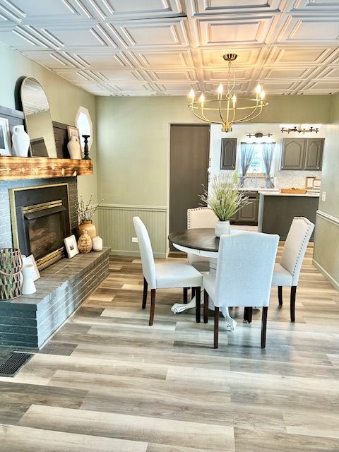 Dining room with a fireplace, round table, chairs, and a chandelier; light green walls, wood floors.
