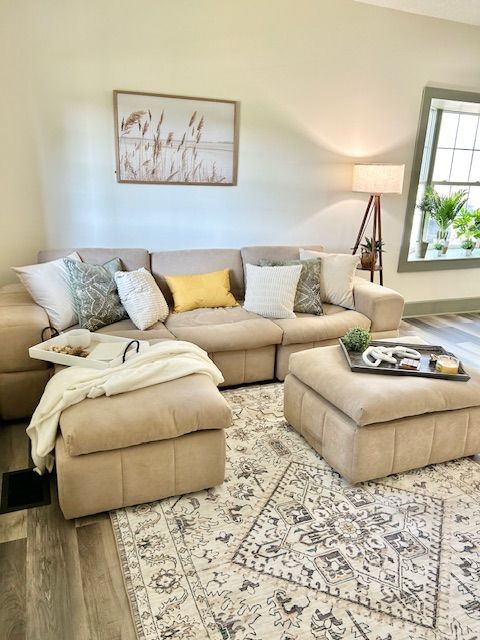 Beige sectional sofa in a living room with patterned rug, pillows, and a wooden framed artwork.
