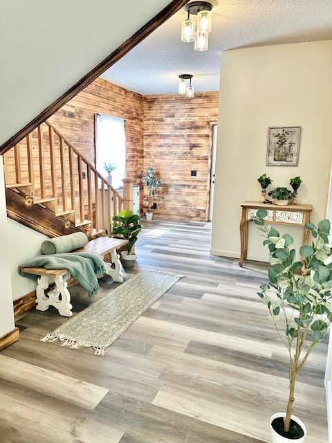 Entryway with wood plank accent wall, staircase, bench, and console table with greenery. Gray wood-look flooring.