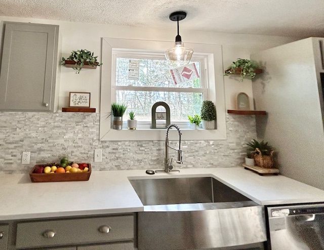 Kitchen with stainless steel sink, white countertops, gray cabinets, and a decorative backsplash.