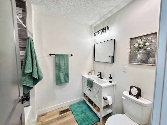 A small, white bathroom with turquoise accents: towel, rug. White vanity with black faucet and mirror. Floral art.