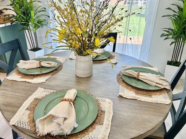 Round table set for four with green plates, beige napkins, and yellow floral arrangement.