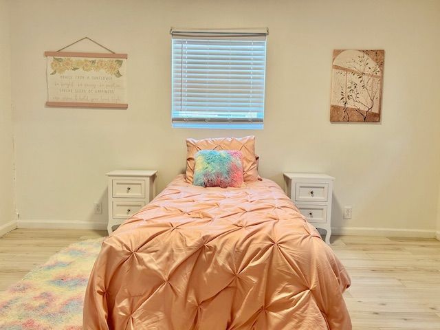 A bedroom with a peach bedspread, rainbow pillow, two white nightstands, and wall art.