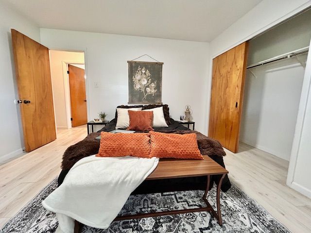 Bedroom with bed, bench, orange pillows, wood doors, and patterned rug.