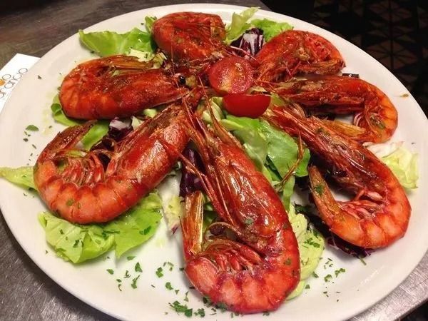 Un piatto con gamberi grigliati disposti a stella su un letto di lattuga fresca, guarnito con pomodorini ciliegino.