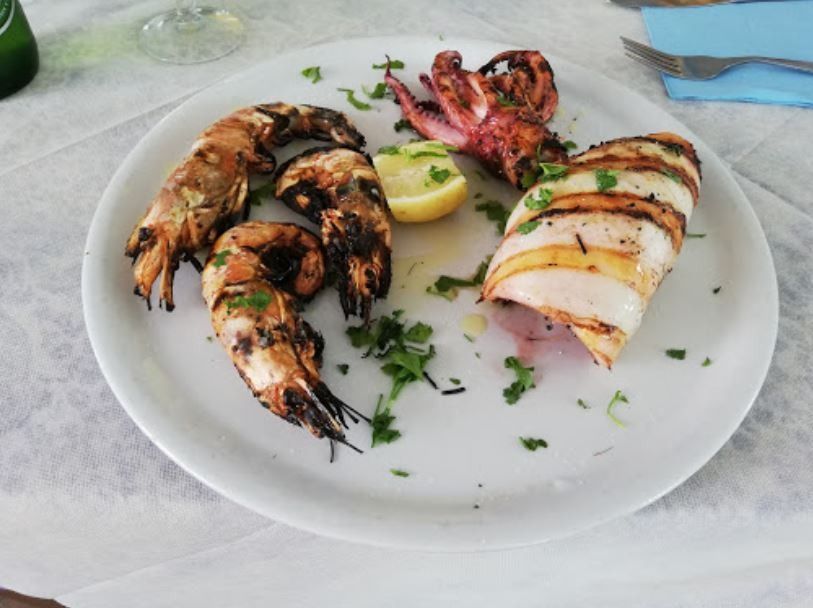 Un piatto bianco con gamberi grigliati, un calamaro intero grigliato e uno spicchio di limone, guarnito con erbe aromatiche.