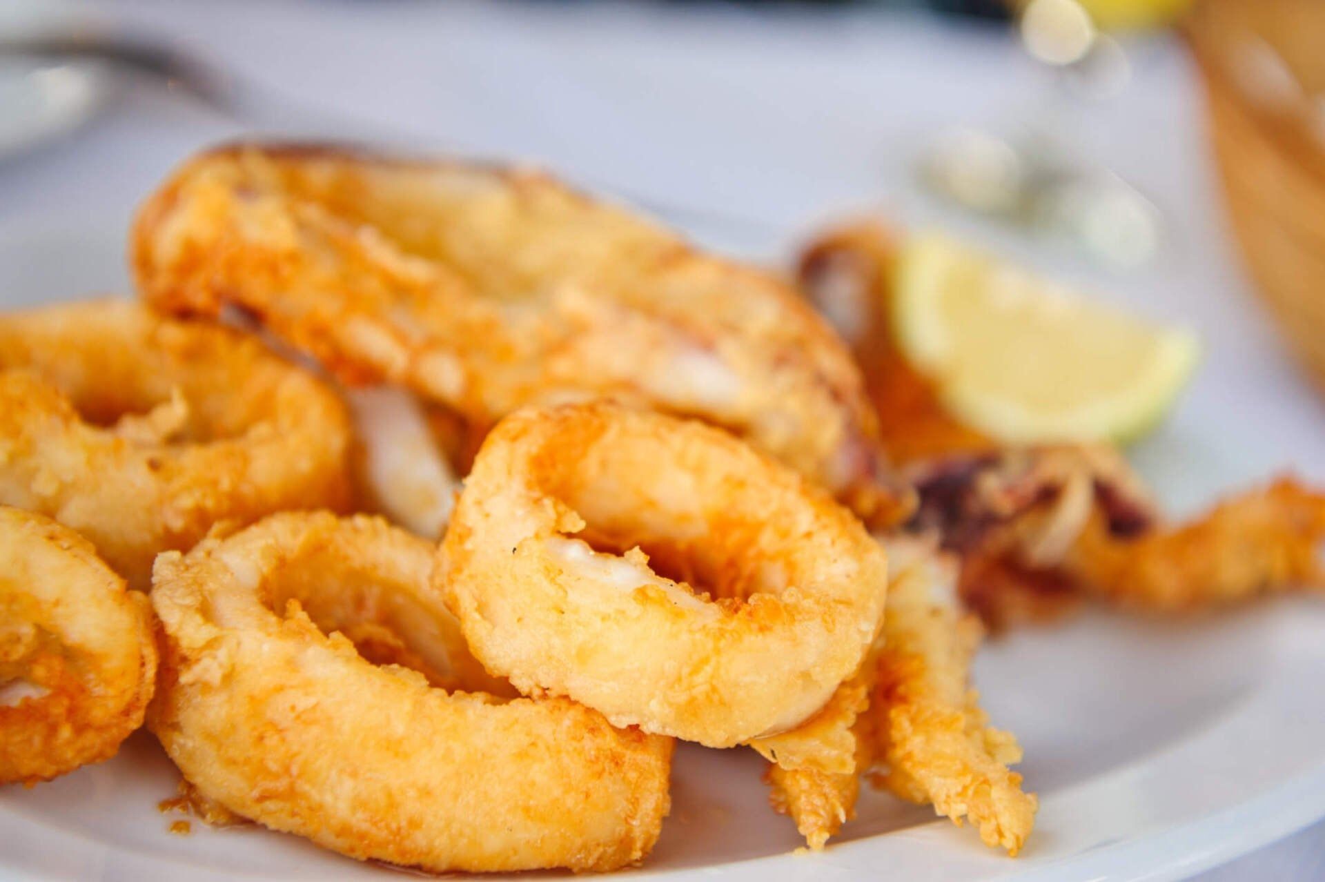 Primo piano di anelli e tentacoli di calamari fritti, dorati e croccanti, serviti su un piatto bianco con uno spicchio di limone.