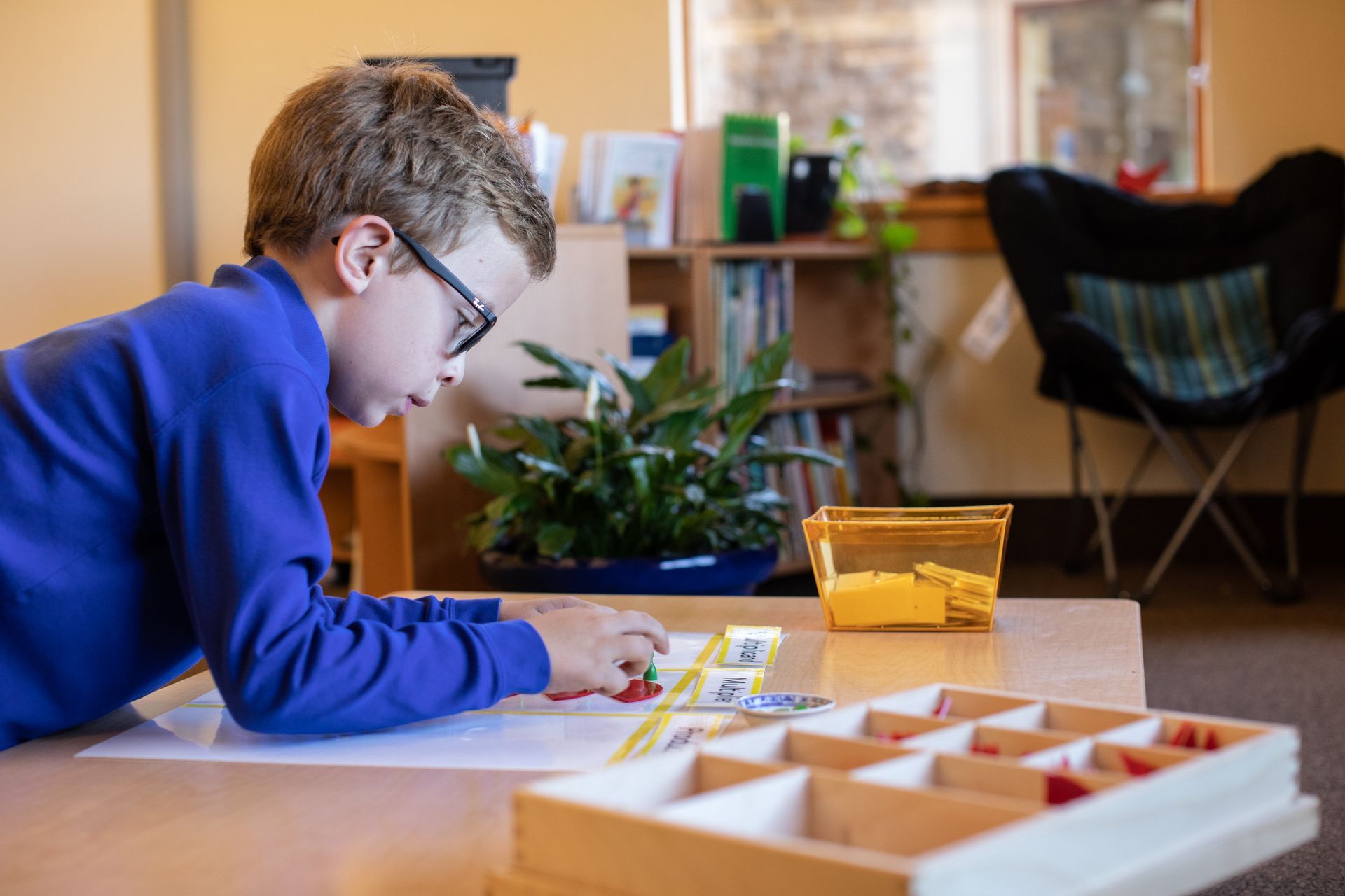 Child in blue sweater working at a table with art supplies and a toy organizer in a living room