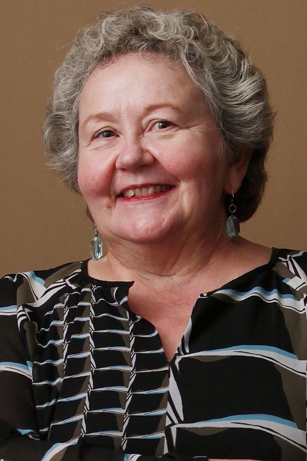 An older woman wearing a striped shirt and earrings smiles for the camera