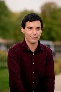 A young man in a maroon shirt is standing in a park.