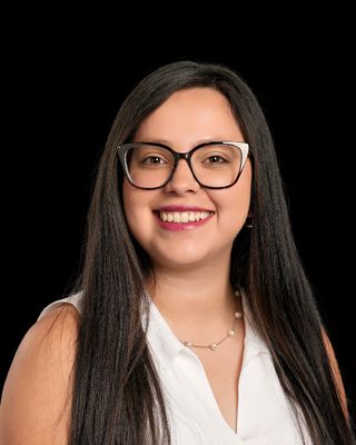 A young man is standing in front of a building with his hands in his pockets.