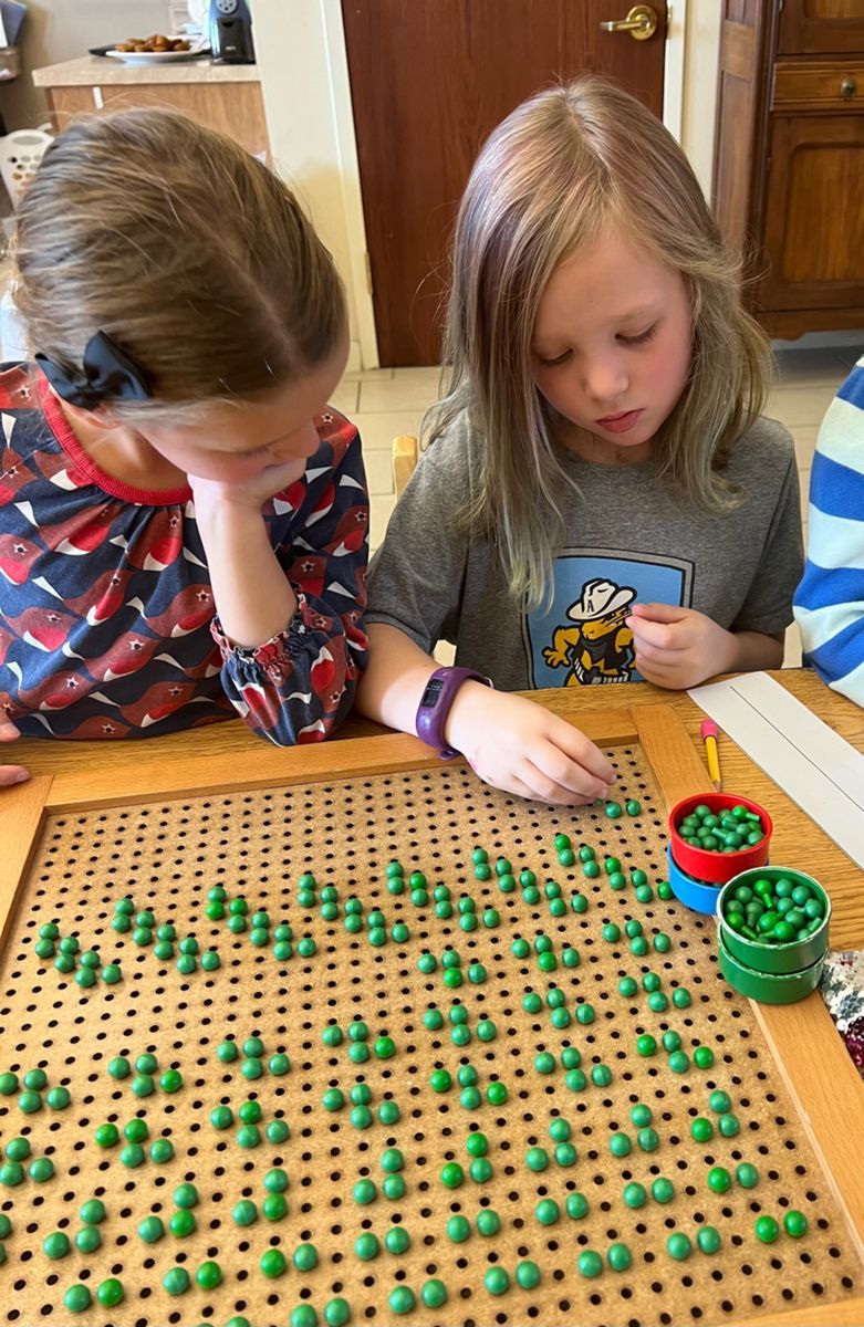 Two young girls are sitting at a table working with montessori math materials.