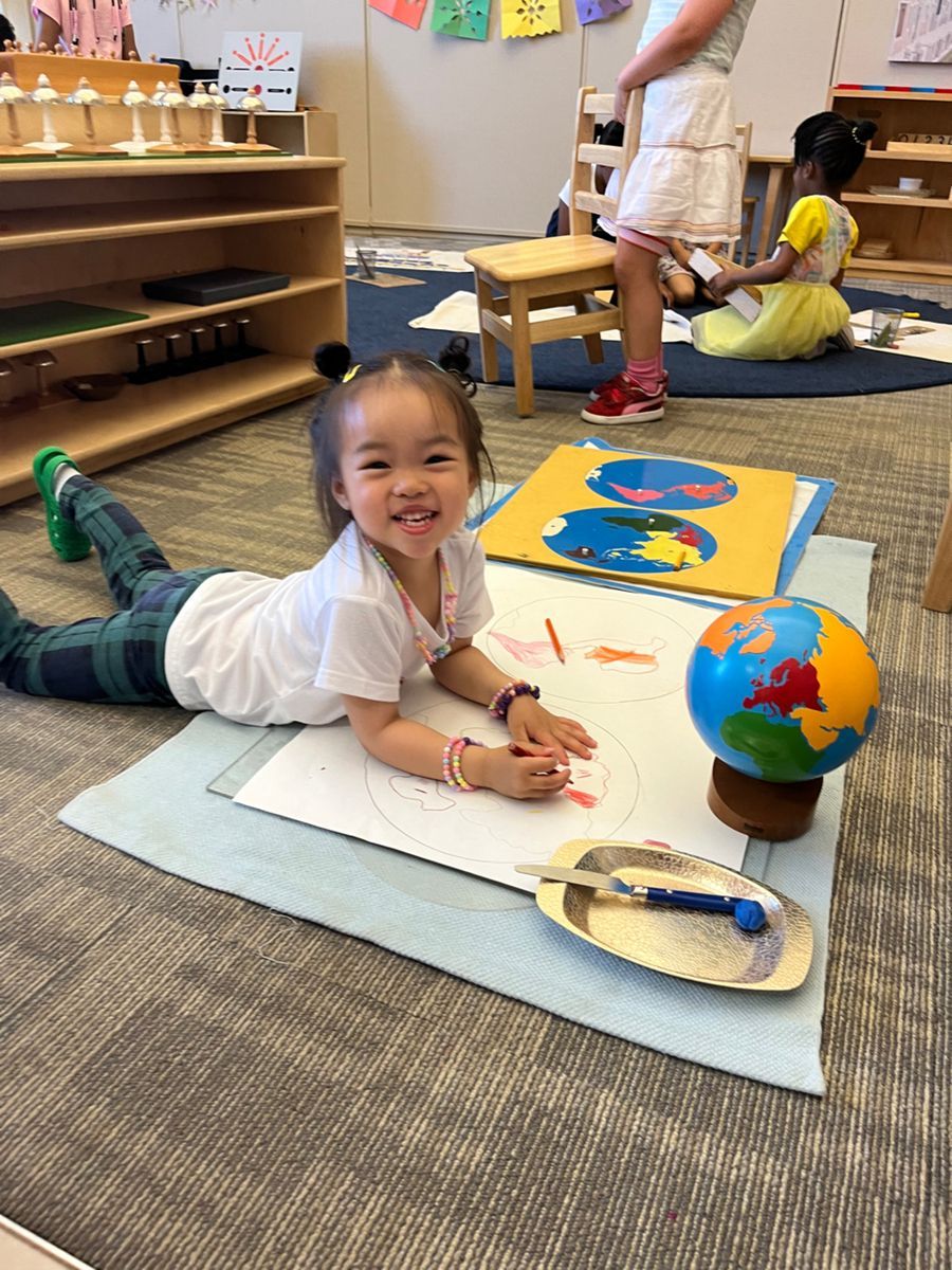 A little girl is laying on the floor painting a picture of the earth.
