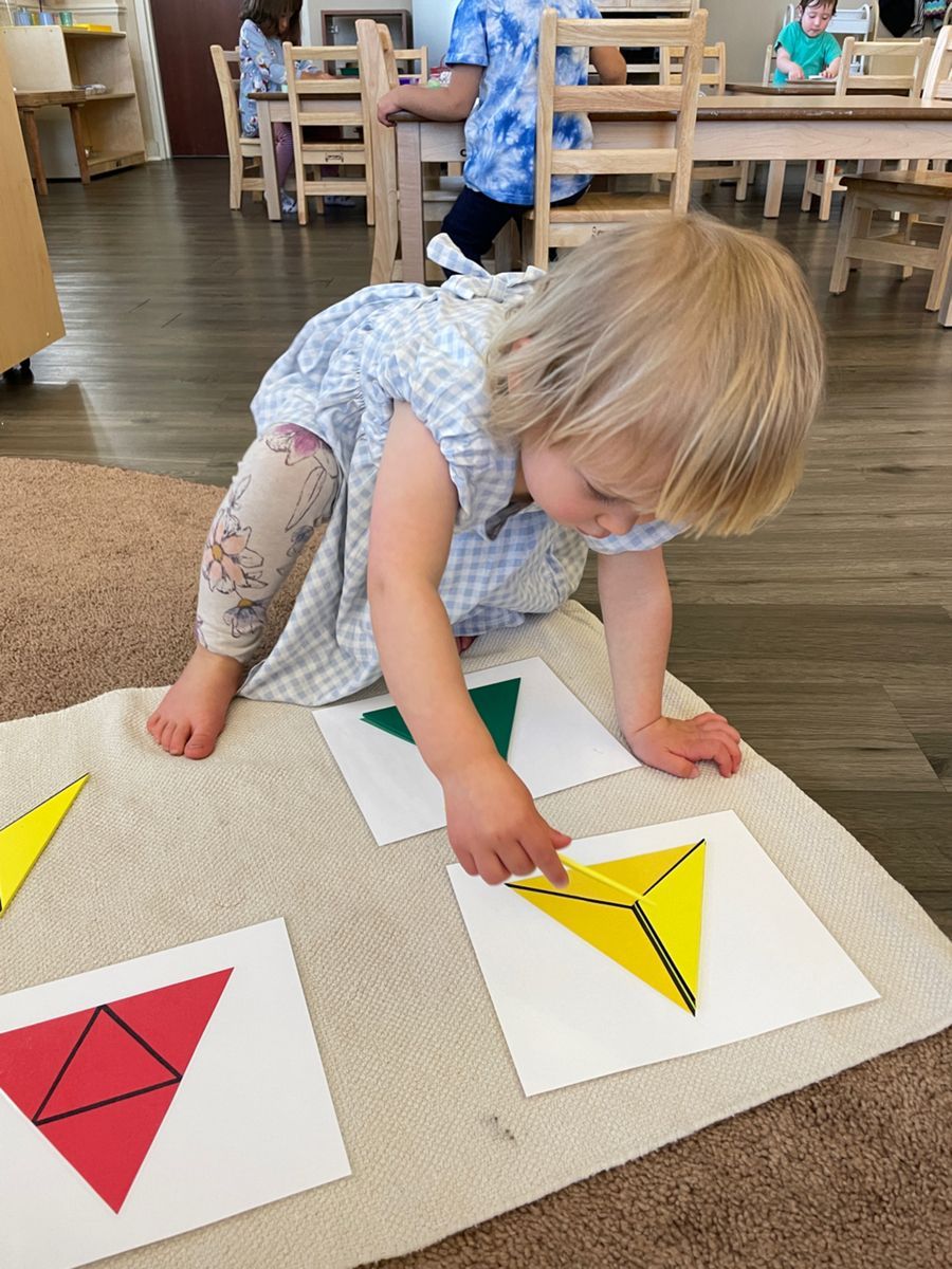 A little girl is playing with triangles on the floor