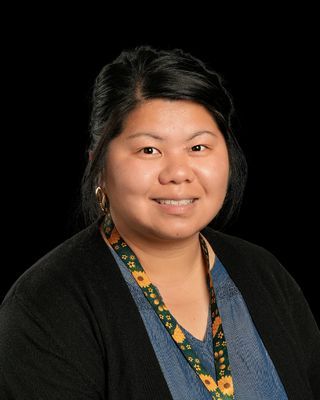 A woman wearing a grey cardigan and a green shirt is smiling for the camera.